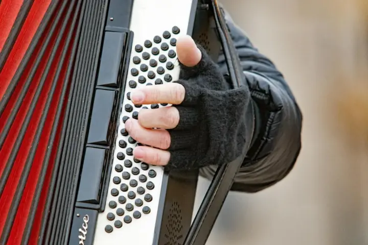 Dłoń w rękawiczce gra na akordeonie, wydobywając dźwięki tego wyjątkowego instrumentu.