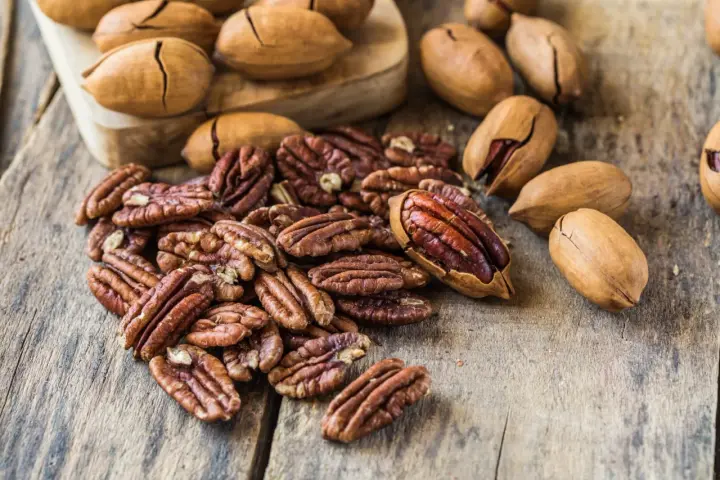 Noix de pécan décortiquées et entières sur fond de bois. Découvrez le noix de pécan bienfait pour une alimentation saine et gourmande.