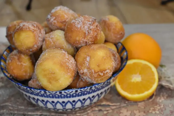 Arancini dolci, soffici arrubiolus di ricotta cosparsi di zucchero, accanto a fette d'arancia.