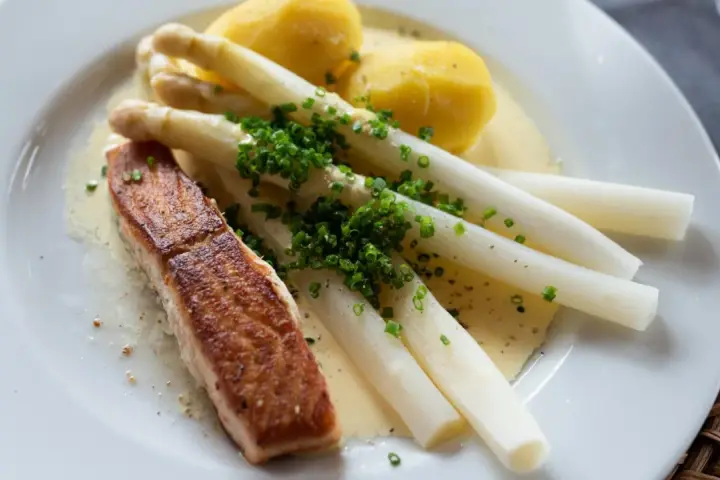 Ein Stück Lachs mit Spargel, Kartoffeln und Sauce Hollandaise. Der Spargel ist mit Schnittlauch bestreut.