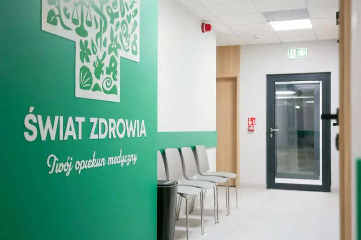 Zielona ściana z napisem "Świat Zdrowia", rząd krzeseł i drzwi w poczekalni kliniki.