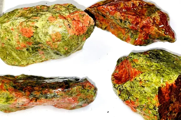 Quattro pezzi grezzi di unakite, con le loro vibranti sfumature verdi e rosse, mostrano le loro proprietà naturali.