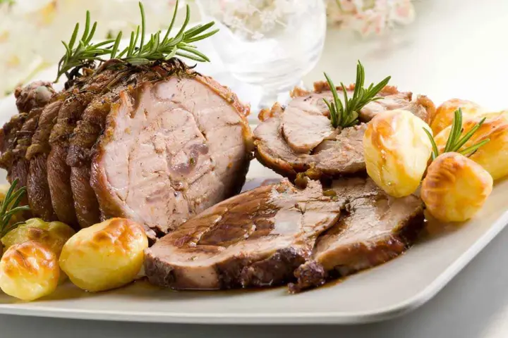 Succulento arrosto di vitello affettato, guarnito con rosmarino e accompagnato da patate arrosto dorate.