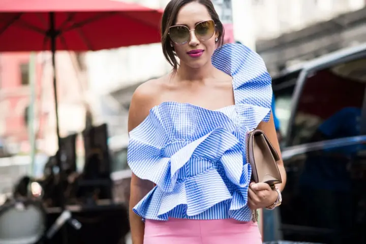 Eleganza in **abbinamento rosa e blu**: top a balze a righe azzurre e bianche con pantaloni rosa cipria, occhiali da sole e borsa a tracolla.