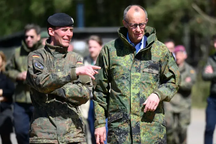 Dwóch mężczyzn w mundurach wojskowych, jeden z flagą Polski, drugi z napisem "MERZ" (Niemcy).