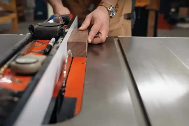 Hands guide a wooden plank along a table saw's fence, demonstrating how to use a table saw for precise cuts.
