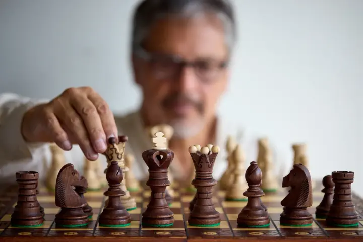 Un homme réfléchit, une pièce d'échecs à la main. Il faut avoir un esprit critique pour anticiper chaque mouvement.