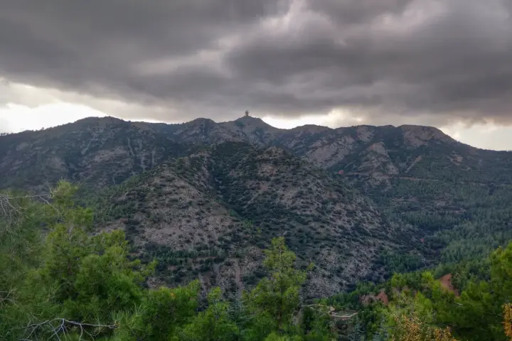 Góry Troodos pod burzliwym niebem. W oddali na szczycie widać charakterystyczną budowlę.