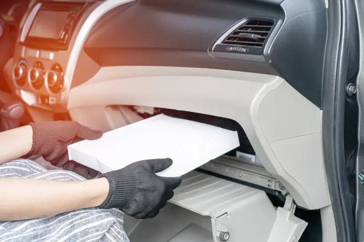 Wymiana filtra kabinowego w Audi A3 8L. Ręce w rękawiczkach wyjmują biały filtr z wnętrza schowka.
