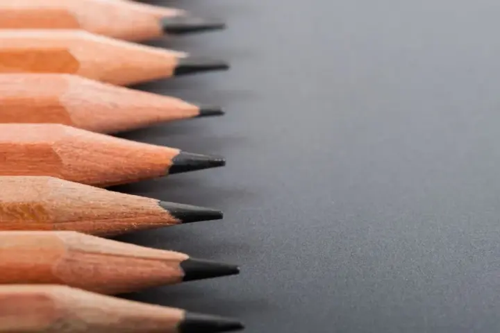 Filas de lápices de madera con puntas afiladas, listos para dibujar. La dureza de los lápices varía, ofreciendo distintas tonalidades.