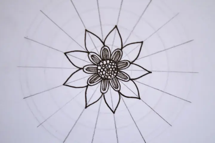 Kwiatowa mandala, rysowana czarnym tuszem, z delikatnymi okręgami i promieniami.