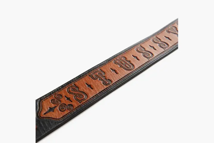 Cintura in pelle marrone con logo Stussy inciso e dettagli decorativi.