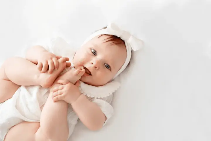La bebé Cora, con su diadema de lazo blanco, juega con sus pies.