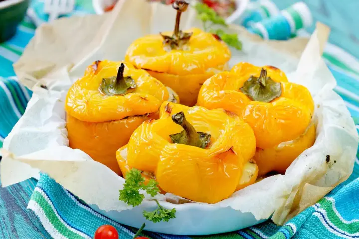 Quatre poivrons farcis jaunes, dorés et appétissants, servis dans un plat garni de papier sulfurisé et décorés de persil frais.