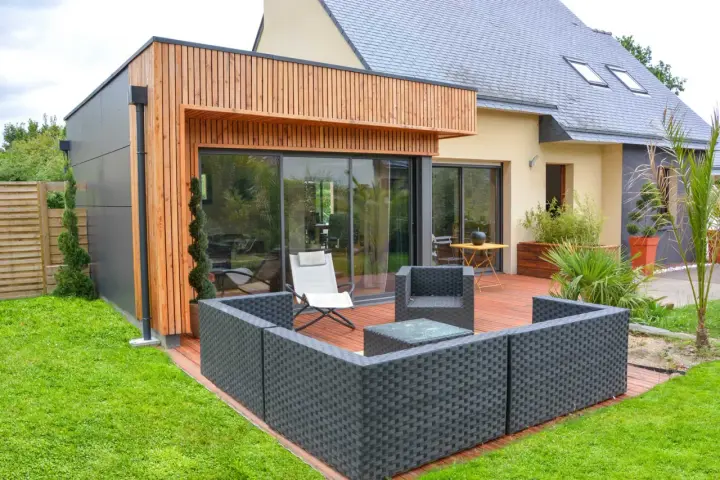 Agrandissement maison ossature bois avec terrasse moderne et mobilier extérieur.