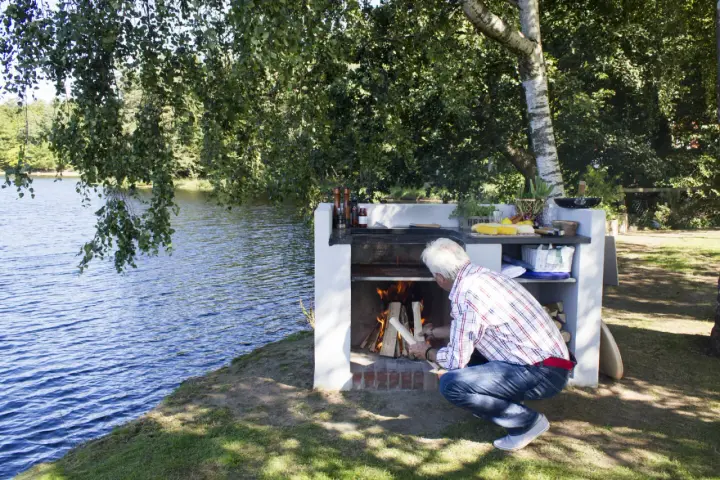 Man tänder en brasa i en nybyggd grill av tegelstenar vid en sjö.