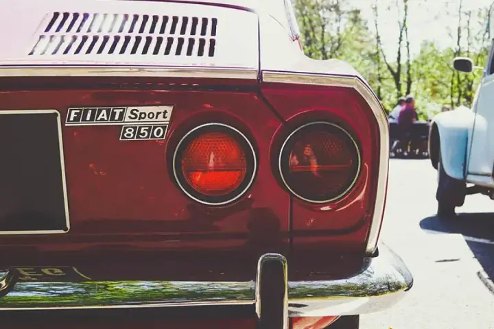 Dettaglio posteriore di una Fiat Sport 850 rossa, con i suoi iconici fanali rotondi. Un pezzo di storia automobilistica, un vero art 102 cds.