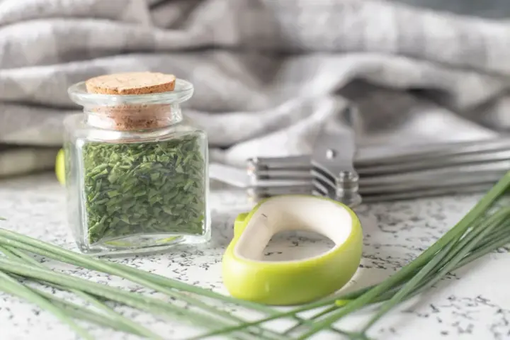 A jar filled with dried chives, showcasing how to dry chives for long-term storage. Fresh chives and kitchen tools are nearby.