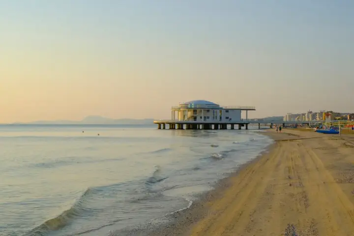 Alba dorata sul mare di Senigallia, con il celebre edificio sul mare e la spiaggia che si estende verso la città.