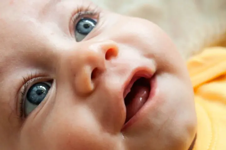 Bebé con ojos azules y boca abierta, mostrando las encías y los primeros dientes saliendo.