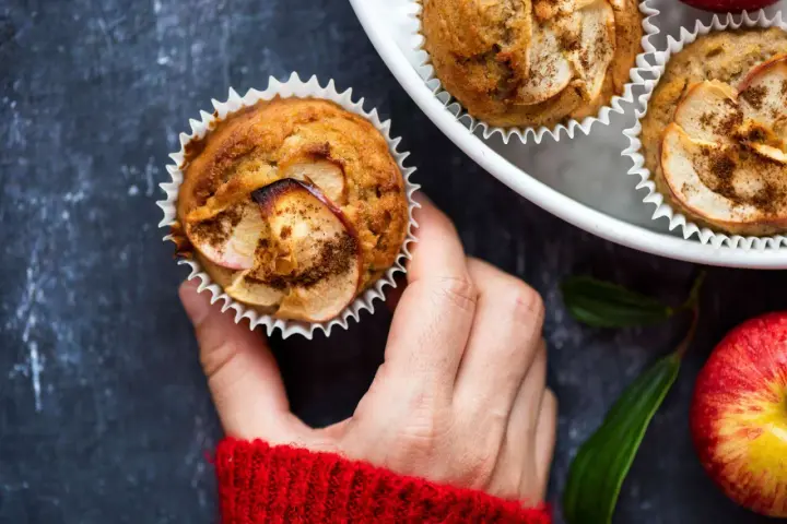 Hand hält einen frisch gebackenen Apfelmuffin, bestreut mit Zimt. Ein tolles Apfelmuffins Rezept!