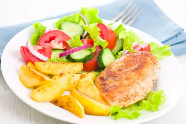Petto di pollo in friggitrice ad aria, patate arrosto e insalata fresca con pomodori, cetrioli e cipolla rossa.