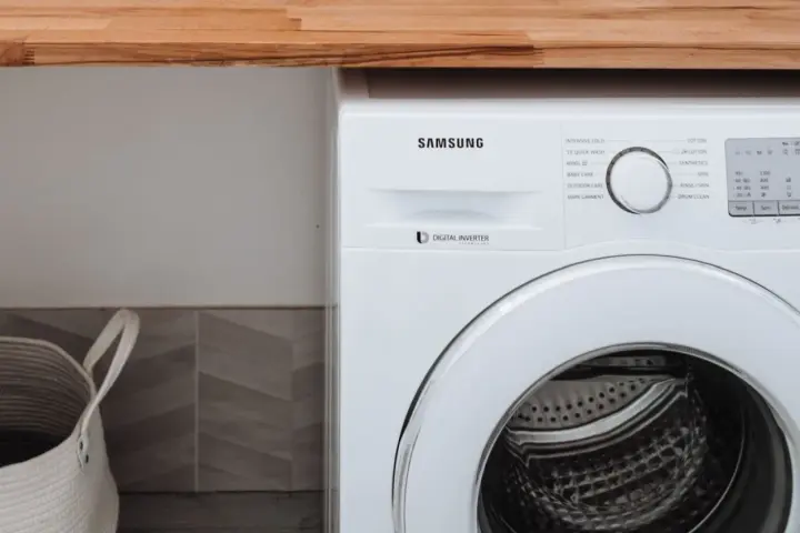 Biała pralka Samsung z technologią Digital Inverter. Obok kosz na pranie.