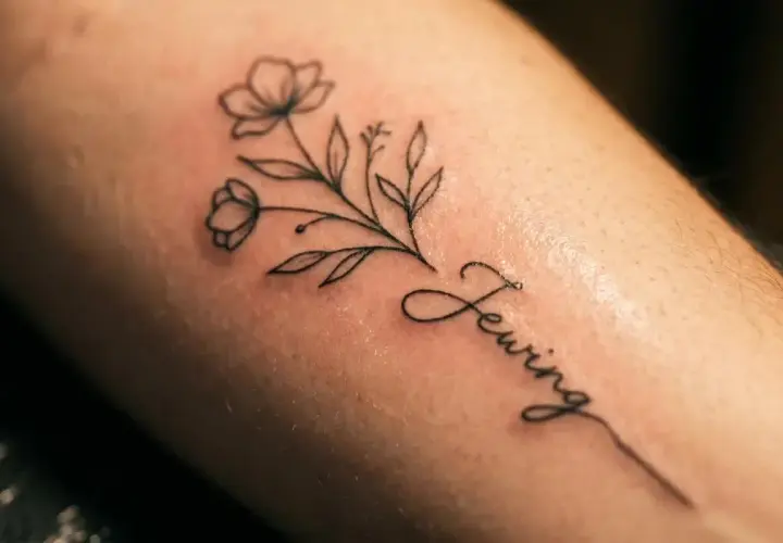 Delikatny line art tattoo z gałązką kwiatów i napisem "Sewing".