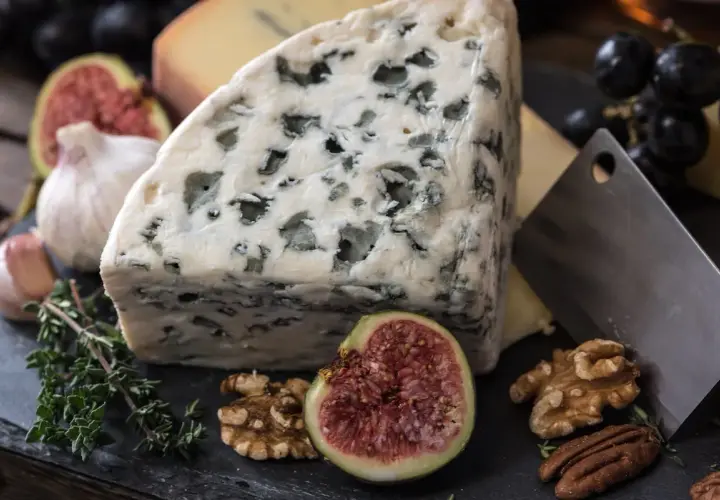 Kawałek ser gorgonzola z niebieską pleśnią, obok figa, orzechy, czosnek i winogrona.