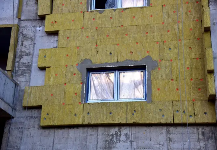 Pannelli isolanti gialli fissati con chiodi rossi mostrano come funziona il cappotto termico su un edificio in costruzione.