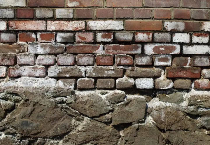 Alte Ziegelwand mit deutlichen Spuren von Salpeter. Die unteren Steine sind grob behauen und bilden eine solide Basis.