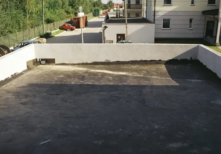 Widok na płaski dach z widocznymi etapami odwodnienia. W tle budynki i drzewa.