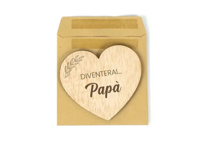 Cuore di legno con scritta "Diventerai... Papà", un dolce annuncio di gravidanza in una busta marrone.