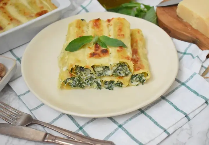 Pyszne cannelloni ze szpinakiem, zapieczone pod beszamelem i serem, ozdobione listkiem bazylii.