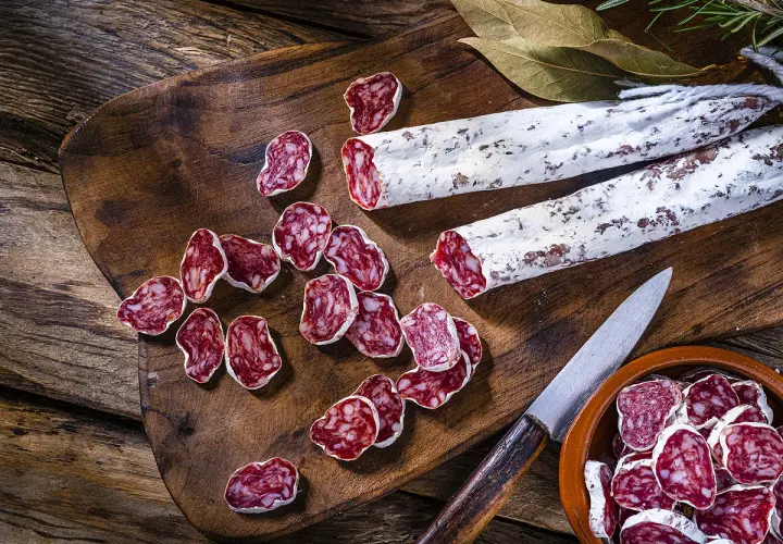Tranches de saucisson sec, entiers et coupés, sur une planche en bois. On peut cuire du saucisson sec pour le déguster chaud.