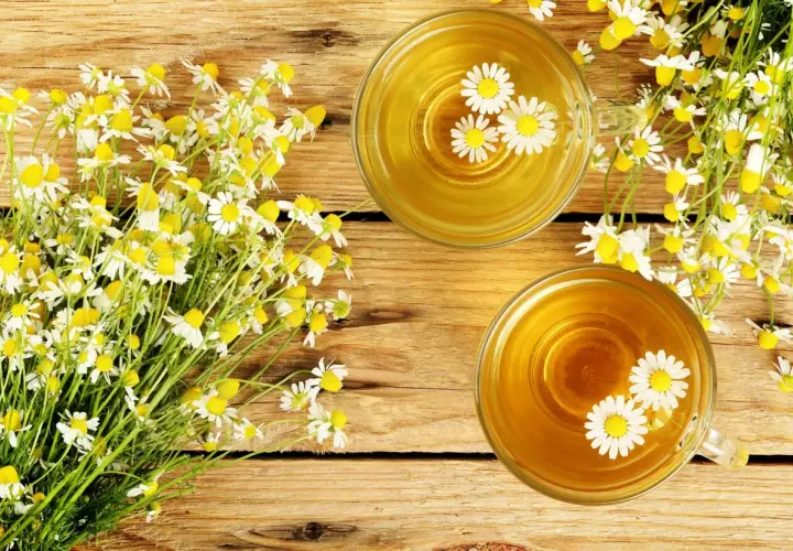 Due tazze di tisana dorata con fiori di camomilla galleggianti, accanto a un mazzo di fiori freschi. Rimedio naturale per il bruciore di stomaco.