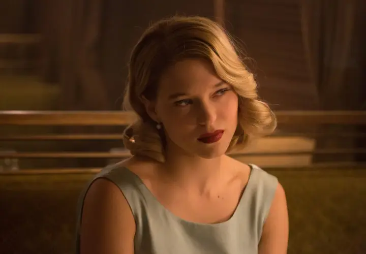 Léa Seydoux w eleganckiej sukience, z burzą blond włosów i czerwoną szminką, przypomina postać z jej filmów.