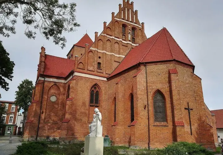 Majestatyczny kościół w Pucku z cegły, z czerwonym dachem i rzeźbą Matki Boskiej.