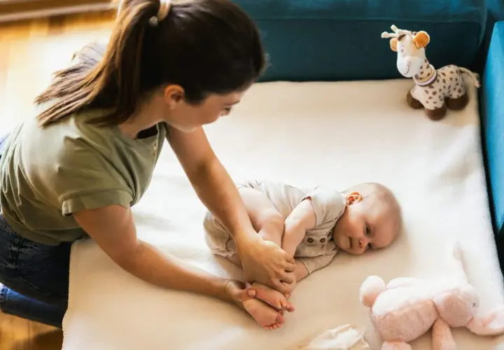 Mama delikatnie masuje nóżki niemowlaka, ucząc się, co robić z niemowlakiem. Obok pluszowa żyrafa i króliczek.