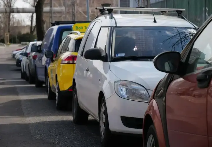 Rząd samochodów, w tym żółty Bolt Taxi, zaparkowany na chodniku.
