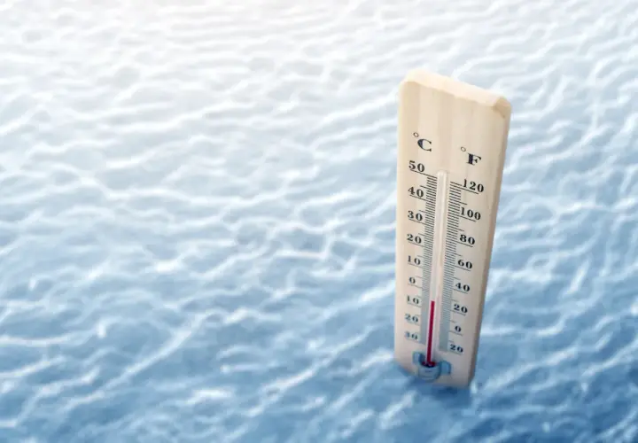 Drewniany termometr pokazuje, że ile stopni ma Bałtyk w sierpniu, wskazując ok. 20°C. Woda jest lekko falująca.