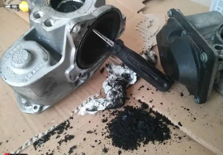 Zdemontowany zawór EGR Audi A4 B8 2.0 TDI z widocznymi objawami zanieczyszczenia sadzą. Narzędzie do czyszczenia.
