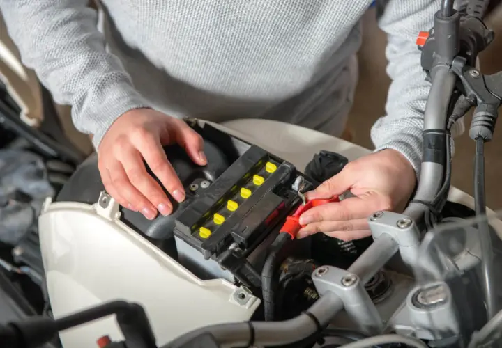 Ręce podłączają kable do akumulatora motocyklowego, szukając odpowiedzi, dlaczego akumulator się rozładowuje.