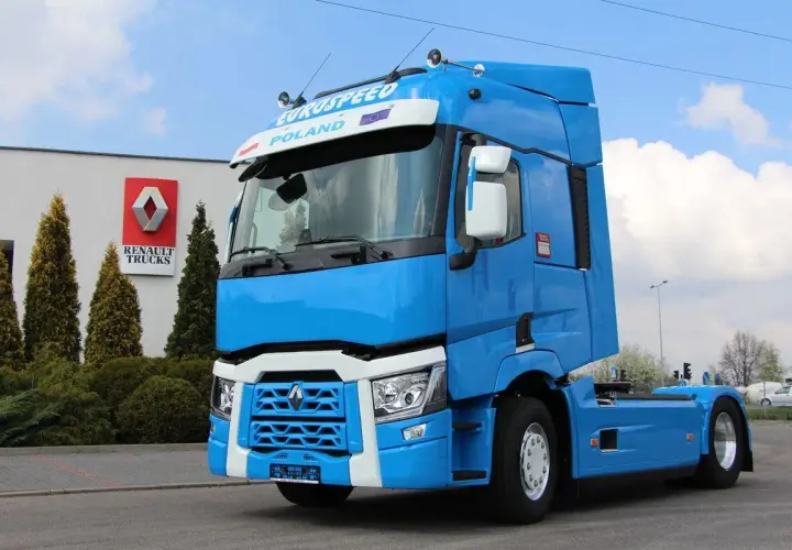 Błękitny ciągnik siodłowy Renault Trucks, jeden z nowoczesnych renault modele, stoi przed budynkiem z logo marki.
