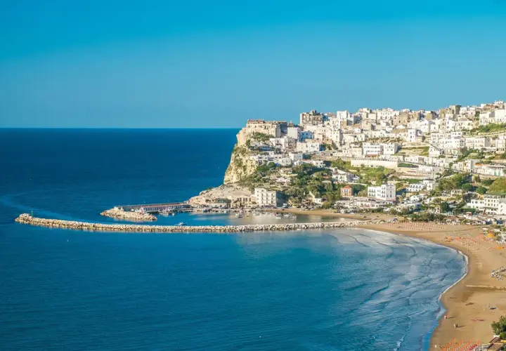 Vue panoramique de Peschici, Italie, avec ses maisons blanches perchées sur la falaise, sa plage de sable fin et son port pittoresque.