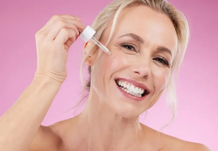 Glad kvinna applicerar serum, oroar sig inte för niacinamide biverkningar.