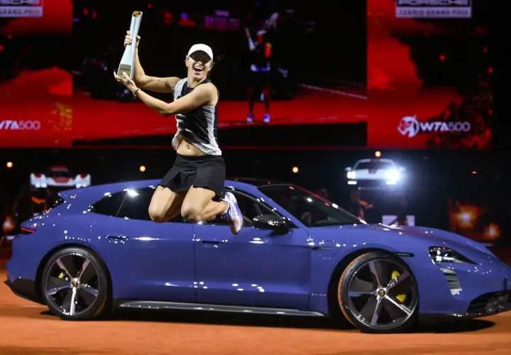 Iga Świątek skacze z pucharem na dachu niebieskiego Porsche, świętując zwycięstwo.