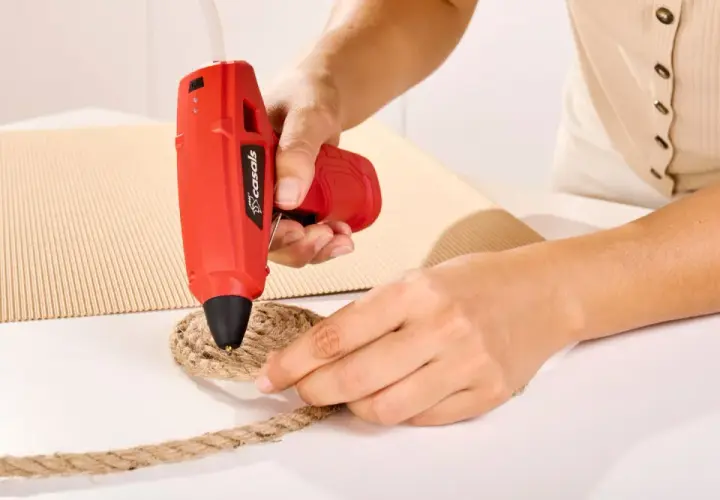 Persona usa pistola de silicona roja para pegar cuerda a cartón. Así es como funciona la pistola de silicona.