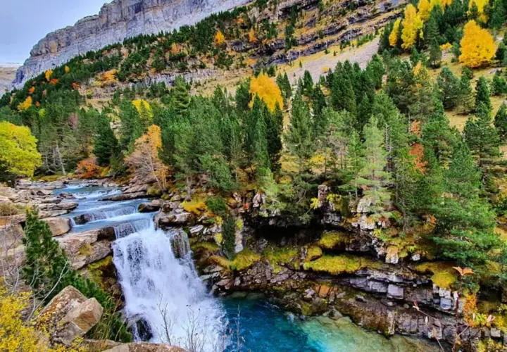 Cascada y río en la ruta Cola de Caballo, rodeados de bosques otoñales y montañas imponentes.