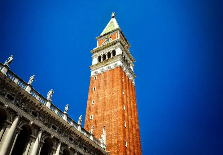 Le campanile de Venise se dresse fièrement sous un ciel bleu éclatant, orné de statues sur son flanc.